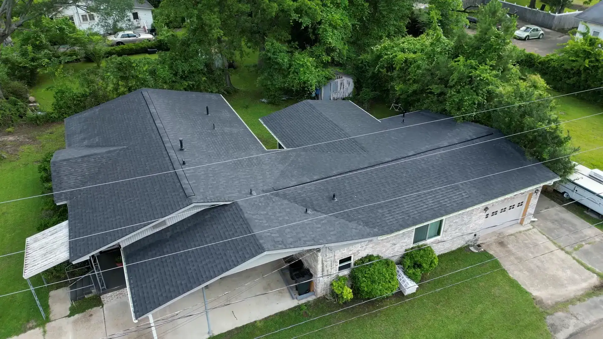 Aerial view of a wide dark shingle roof on a stone ranch home in a mature southwest Arkansas neighborhood